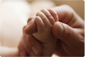 A newborn baby's hand grasps the finger of an adult