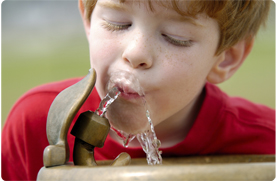 a young boy drinks from a water fountain